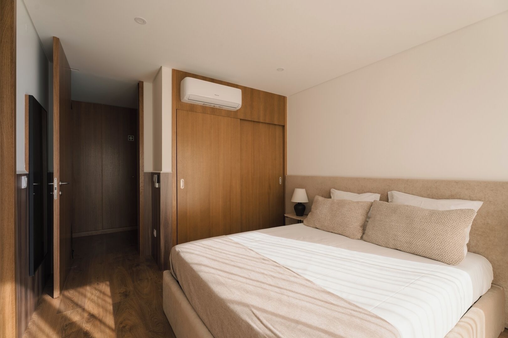 A bedroom with a bed, wooden wardrobe, and an air conditioning unit.