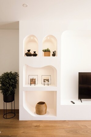 A modern interior with a white wall, a black floor lamp, a potted plant, and a TV on a stand.