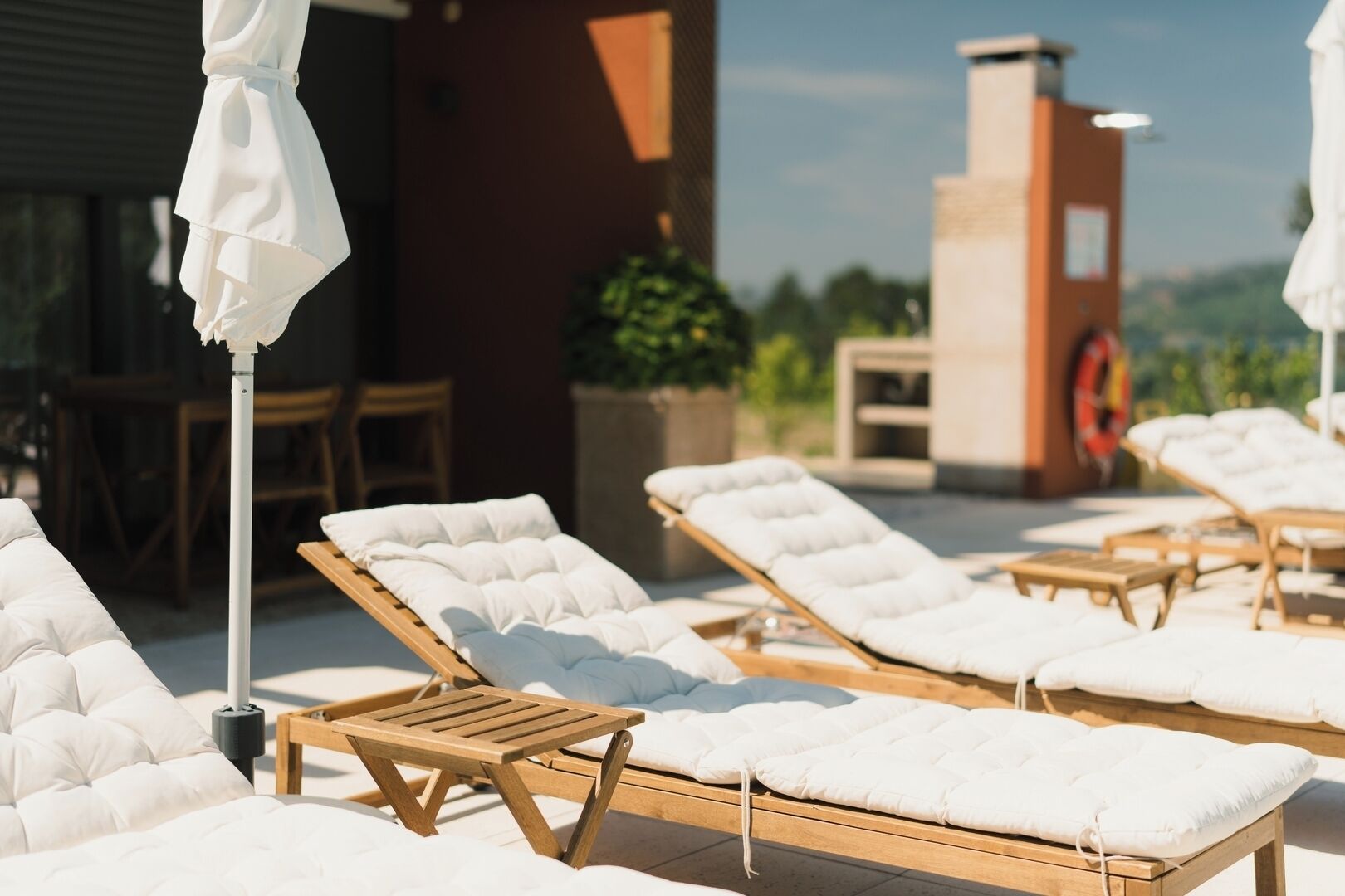 Una terraza con sillones de sol, una mesa y sombrillas.