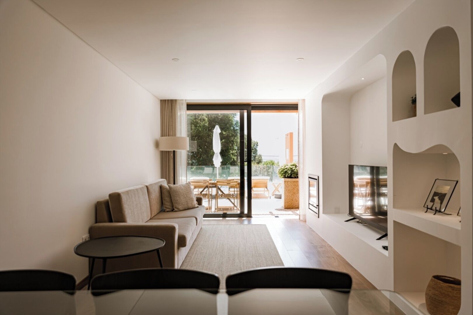 Una sala de estar moderna con un sofá, una mesa de centro, televisor y un balcón con mobiliario exterior.