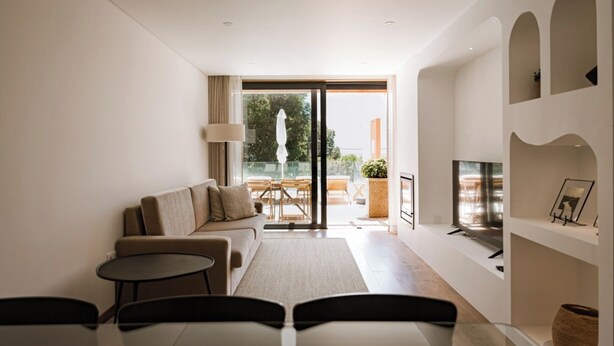 En moderne stue med sofa, sofabord, TV og en balkon med udendørs møbler.