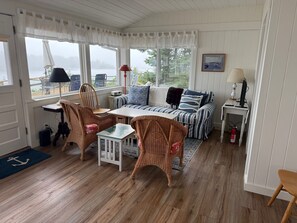 Una habitación acogedora con piso de madera, un sofá a rayas, sillas de mimbre, una mesita y un escritorio para computadora.