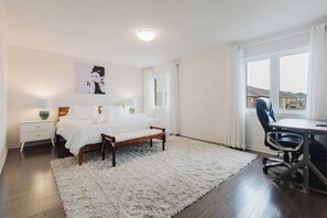 Ein Schlafzimmer mit Bett, Nachttischen, einem Schreibtisch mit Stuhl, einem großen Fenster und einem Bild an der Wand.