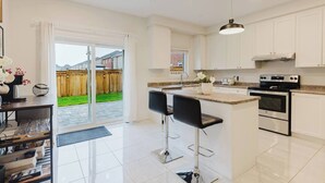 A modern kitchen with a large island, stainless steel appliances, and a sliding glass door leading to a backyard. - Spacious 4BR Retreat | Backyard | Near Ontario (Oshawa)