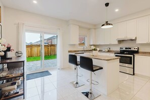 A modern kitchen with a large island, stainless steel appliances, and a sliding glass door leading to a backyard. - Spacious 4BR Retreat | Backyard | Near Ontario (Oshawa)