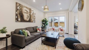 A living room with a sofa, coffee table, and a Buddha painting. - Spacious 4BR Retreat | Backyard | Near Ontario (Oshawa)