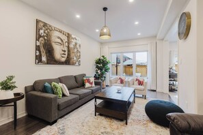A living room with a sofa, coffee table, and a Buddha painting. - Spacious 4BR Retreat | Backyard | Near Ontario (Oshawa)