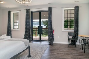 A hotel room with a bed, a small table, two chairs, a window with curtains, and a view of the outdoors. - The Factory House at Keuka Lake: Hot Tub, BBQ, Unreal Lake Views, Chef's Kitchen (Hammondsport)