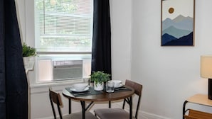 Un coin repas avec une table dressée pour deux personnes, une plante en pot et un tableau accroché au mur.