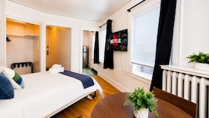 Une chambre d’hôtel avec un lit, un téléviseur fixé au mur, un radiateur et une petite plante sur une table.