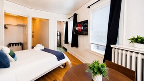 A hotel room with a bed, a TV mounted on the wall, a radiator, and a small plant on a table.