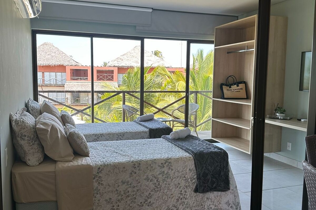 A bedroom with two beds, a large window, and a view of buildings and trees.