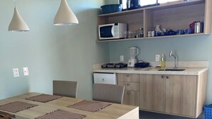 A modern kitchen with wooden cabinets, a dining table with chairs, pendant lights, and a window above the sink.