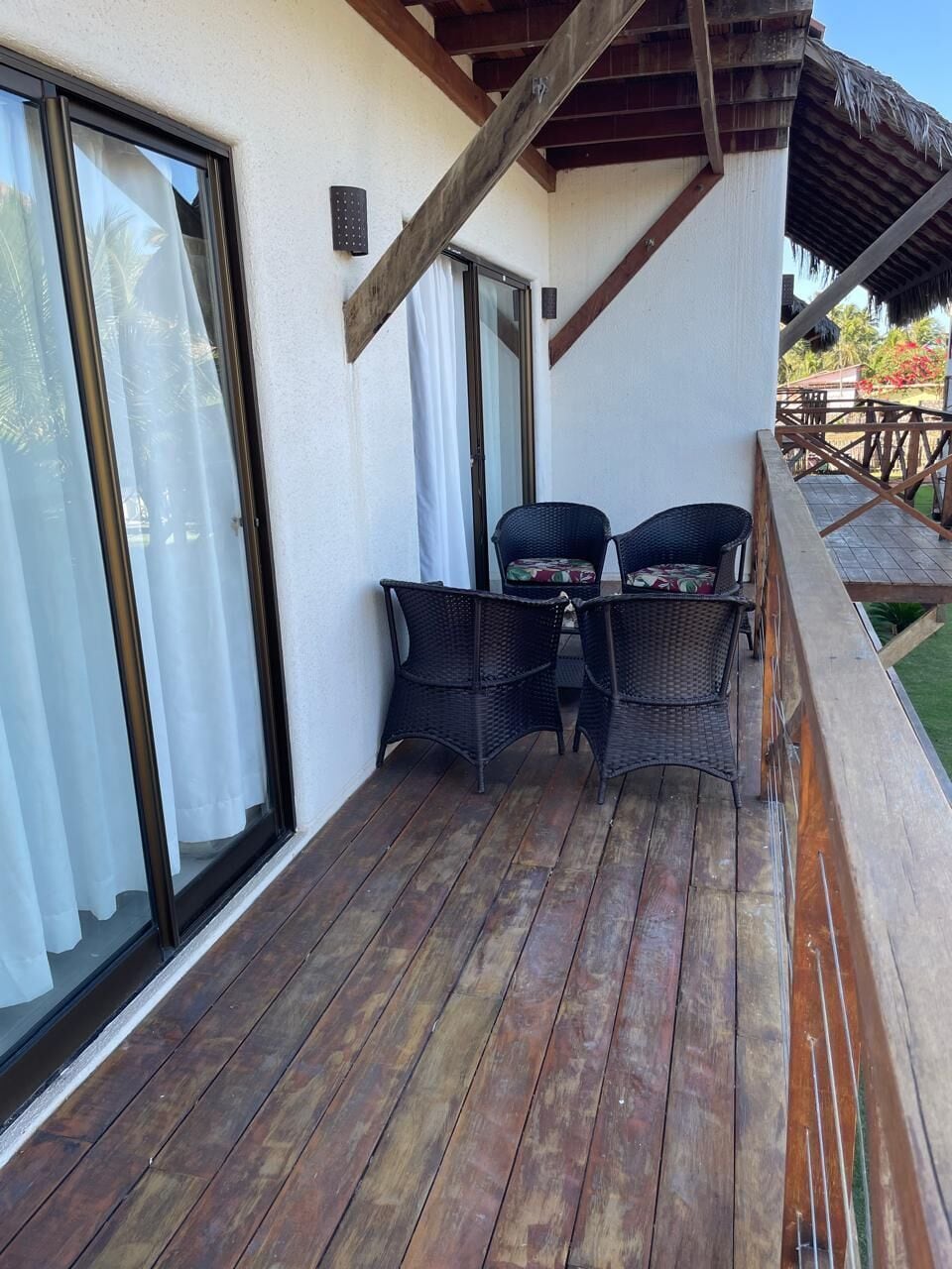 A wooden deck with wicker chairs and a table, a sliding glass door, and a wooden railing.