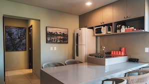 A modern kitchen with a central island, bar stools, a refrigerator, microwave, and a coffee maker.