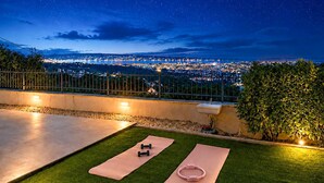 Un área de ejercicio al aire libre con colchonetas y mancuernas, con vistas a un paisaje urbano nocturno.