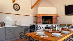 Una cocina con horno de ladrillo, un reloj y una mesa de comedor lista para cuatro comensales.