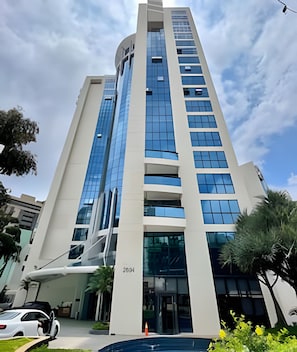 Um edifício alto e moderno com fachada de vidro, entrada destacada e placa de endereço visível.