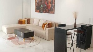 A modern living room with a sectional sofa, a coffee table, a dining table with chairs, and a wall-mounted artwork. - sandra 12 (la soukra)