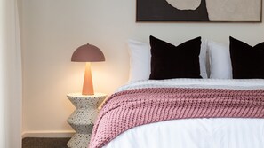 A neatly made bed with a pink knitted blanket, a modern floor lamp, and a simple wall decoration. - Edenbrook in Prahran (Prahran)