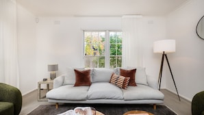 Un salon moderne avec un canapé gris, une lampe sur pied et une fenêtre donnant sur des arbres.
