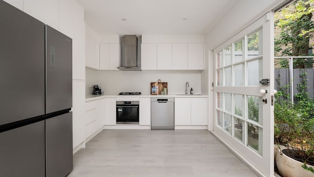 Une cuisine moderne avec des meubles blancs, un réfrigérateur en acier inoxydable, un lave-vaisselle et une cuisinière à gaz.