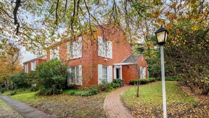 Une maison en briques avec un chemin menant à l’entrée, entourée d’arbres et de verdure.
