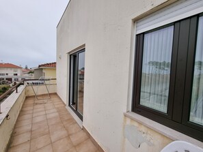 Varanda com cadeira de metal, porta de vidro deslizante e vista para edifícios vizinhos.