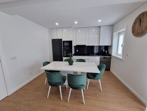 Uma cozinha moderna com armários brancos, uma geladeira preta e uma mesa de jantar com cadeiras verdes.