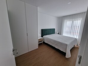 A bedroom with a bed, a nightstand, a wardrobe, and a window with curtains.