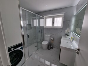 A modern bathroom with a glass-enclosed shower, a toilet, a sink with a mirror, and a washing machine.