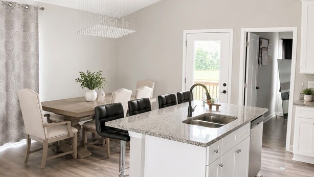 Une cuisine moderne dotée d’un îlot central, de meubles blancs et d’un coin repas avec une table et des chaises.