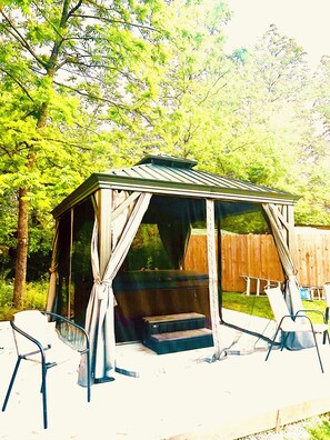 A covered outdoor seating area with a bench and chairs, surrounded by trees. - Spacious 6-bedroom house in tranquil Tracy City with AC (Tracy City)