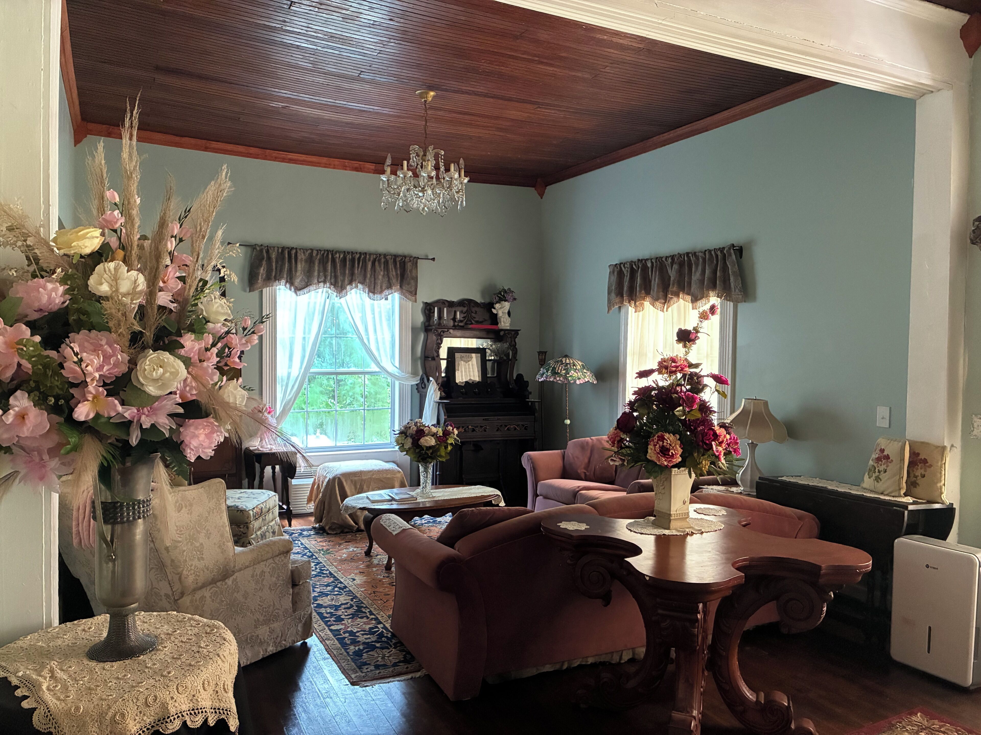 Ein Wohnzimmer mit Holzbalkendecke, einem Chandelier, einem Klavier, einer Couch und einem Tisch mit Blumen.
