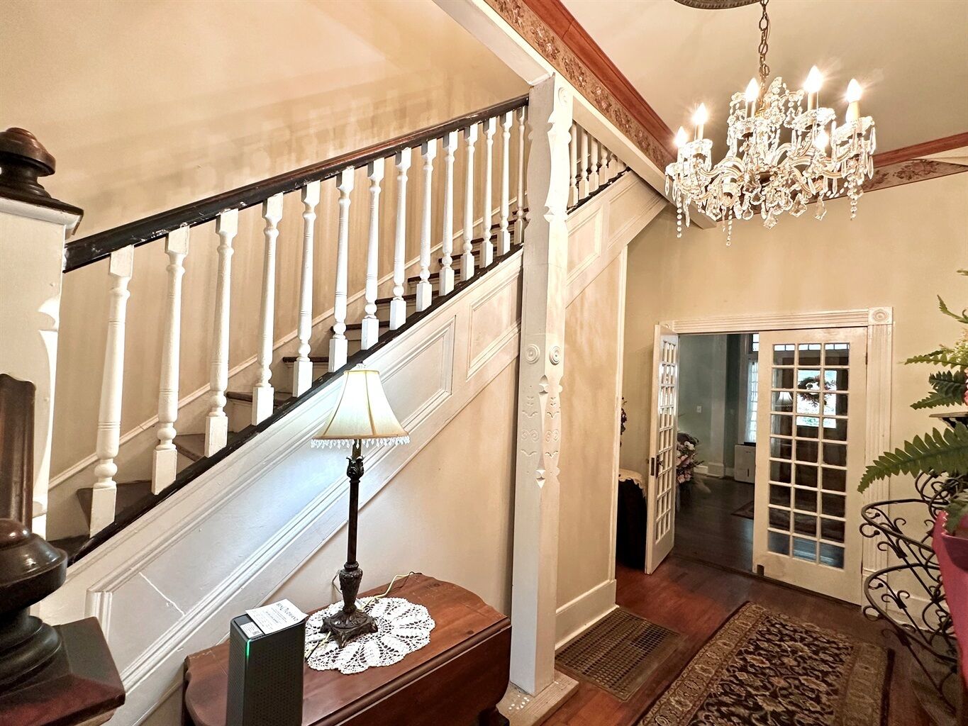 Eine prachtvolle Treppe mit weißen Balustraden, einem Chandelier und einem Tisch mit einer Lampe.