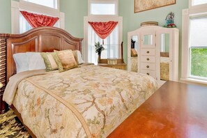 Ein Schlafzimmer mit einem großen Bett, einem Schminktisch, einem Spiegel und einem Fenster mit Vorhängen.