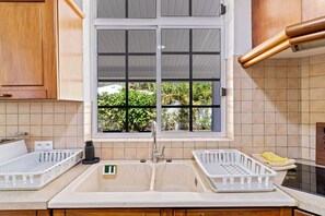 Eine Küche mit doppeltem Spülbecken, Holzschränken, einem Fenster mit Blick auf Grünflächen und einer gefliesten Spritzschutzwand.