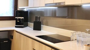 Een moderne keuken met lichte houten kastjes, een zwarte koffiemachine, een messenblok en een wijnrek.
