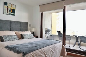 Ein Hotelzimmer mit einem großen Bett, einem Schreibtisch und einem Balkon mit Stühlen.
