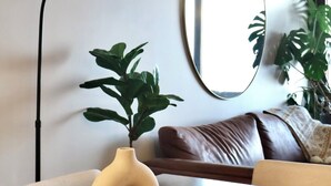 Een moderne woonkamer met een ronde spiegel, een zwarte vloerlamp, een bruine leren bank en een tafel met decoratieve vazen.