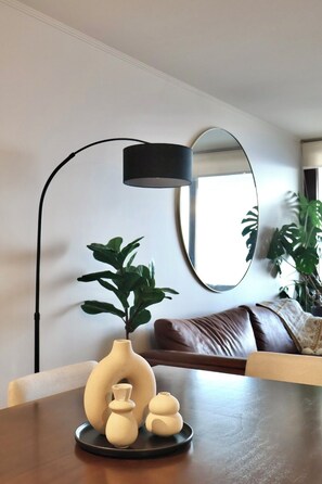 Ein modernes Wohnzimmer mit einem runden Spiegel, einer schwarzen Stehlampe, einem braunen Ledersofa und einem Tisch mit dekorativen Vasen.
