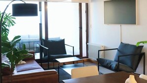 Een moderne woonkamer met een bank, stoelen, een eettafel en een groot raam.