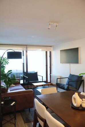 Ein modernes Wohnzimmer mit einer Couch, Sesseln, einem Esstisch und einem großen Fenster.