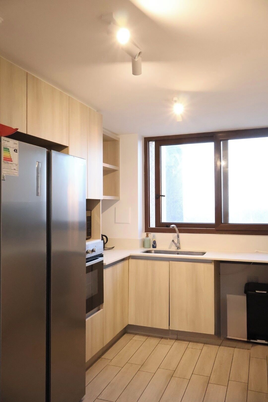 A kitchen with a refrigerator, oven, sink, and window.