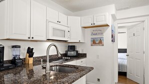A kitchen with white cabinets, a granite countertop, a built-in microwave, a coffee maker, and a sign that says 'Welcome to our Beach House.' - Ocean Block 3BR 2BA | Walk to Beach | Sleeps 8 (Ocean City)