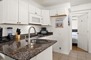 A kitchen with white cabinets, a granite countertop, a built-in microwave, a coffee maker, and a sign that says 'Welcome to our Beach House.' - Ocean Block 3BR 2BA | Walk to Beach | Sleeps 8 (Ocean City)