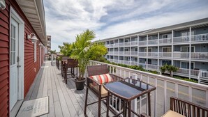 A balcony with wicker furniture, a potted plant, and a clear view of a multi-story building. - Ocean Block 3BR 2BA | Walk to Beach | Sleeps 8 (Ocean City)