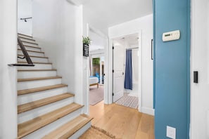 A staircase leading to a bedroom with a bed, a blue door, and a thermostat on the wall. - Harbor Home - Walking Distance to Twin Lakes Beach! (Santa Cruz)