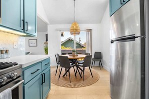 A modern kitchen with teal cabinets, a stainless steel refrigerator, and a dining area with a round table and chairs. - Harbor Home - Walking Distance to Twin Lakes Beach! (Santa Cruz)
