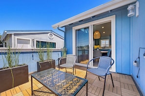 A patio with a glass table and chairs, a sliding glass door, and a view of a neighboring house. - Harbor Home - Walking Distance to Twin Lakes Beach! (Santa Cruz)
